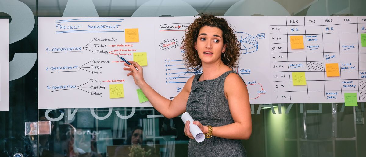 A project manager explaining her day to day roles and responsibilities listed on a whiteboard.